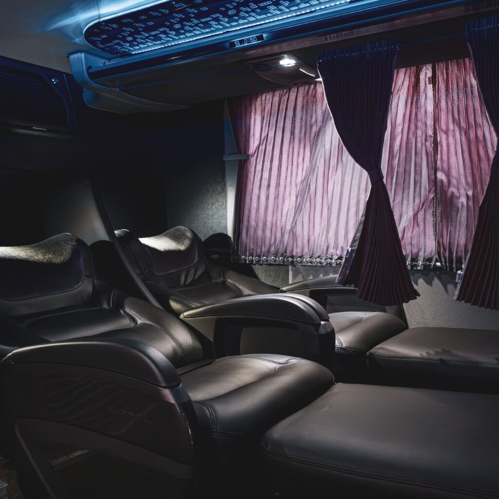 Interior escuro de um veículo de luxo com assentos reclináveis ​​de couro preto e cortinas roxas.