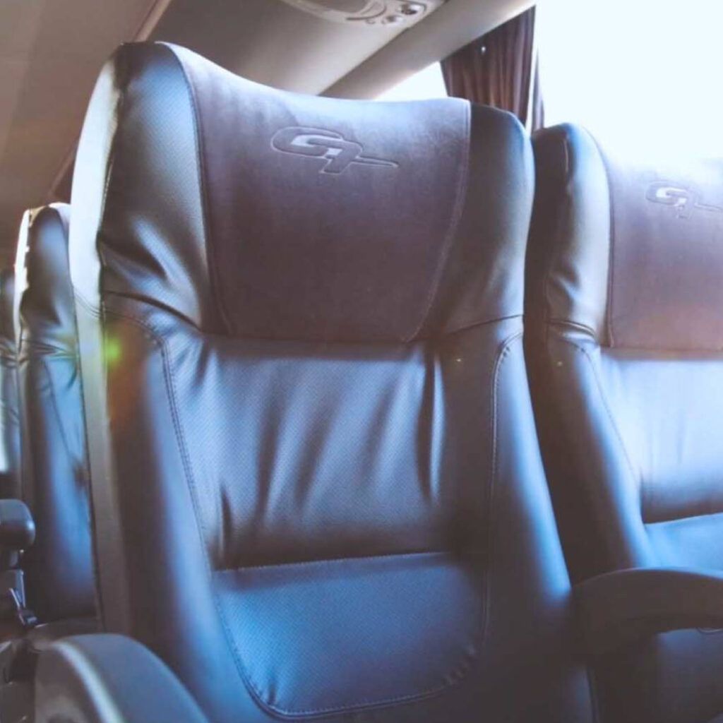 Close-up de assentos de ônibus de couro preto com encostos de cabeça; vista interna, possivelmente para viagem.