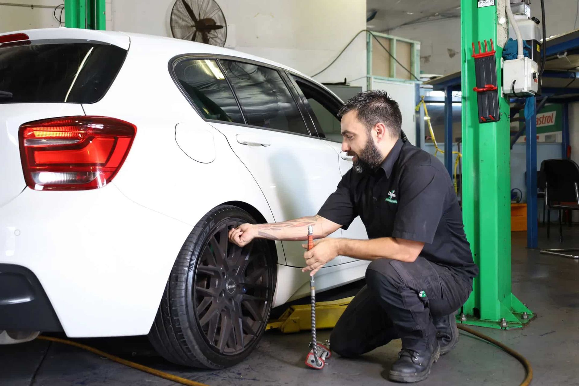 A Man is Kneeling Down Next to a White Car in a Garage — Ultra Tune Nambour In Nambour, QLD