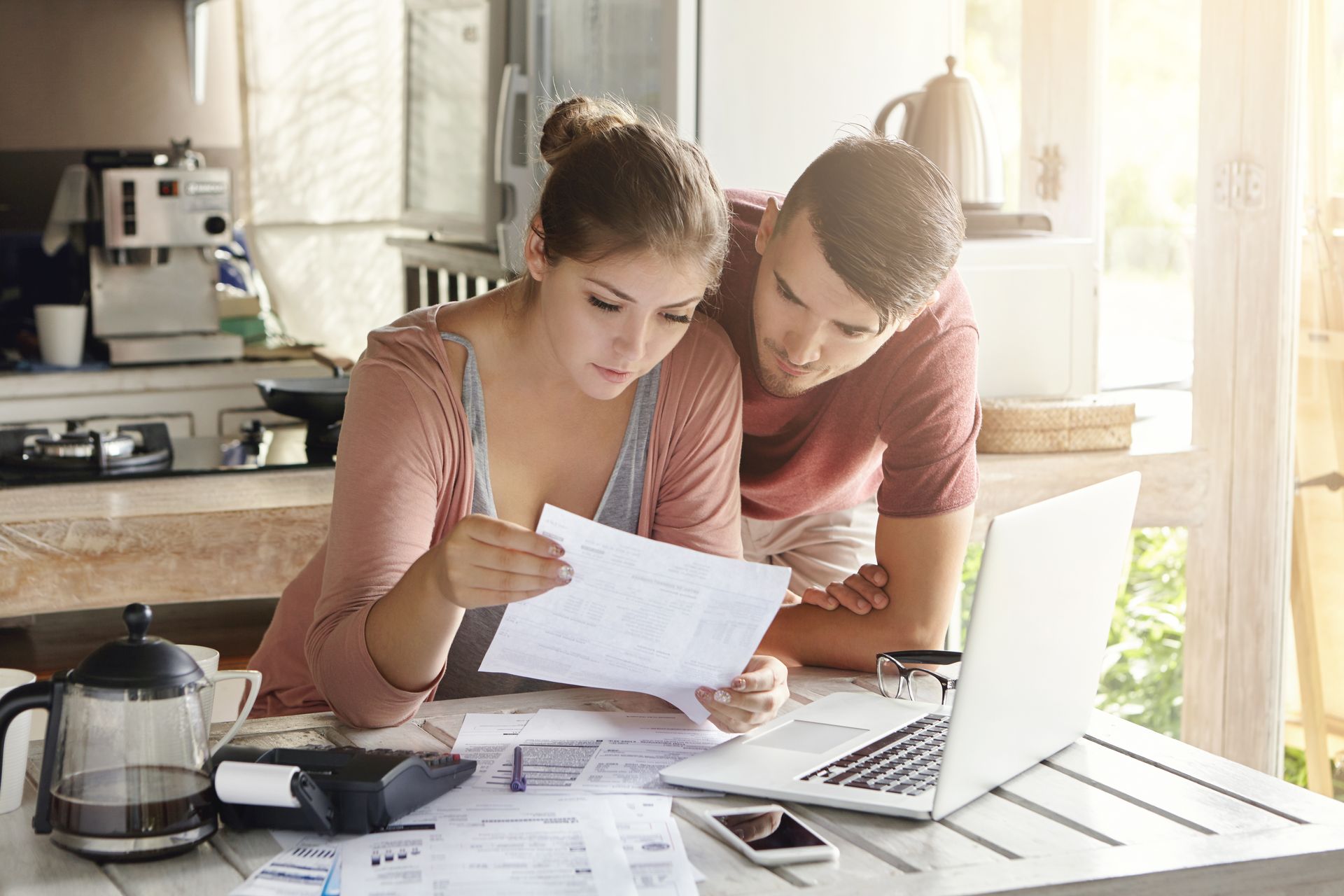 Couple reviewing financial documents and using laptop for online budgeting at home.