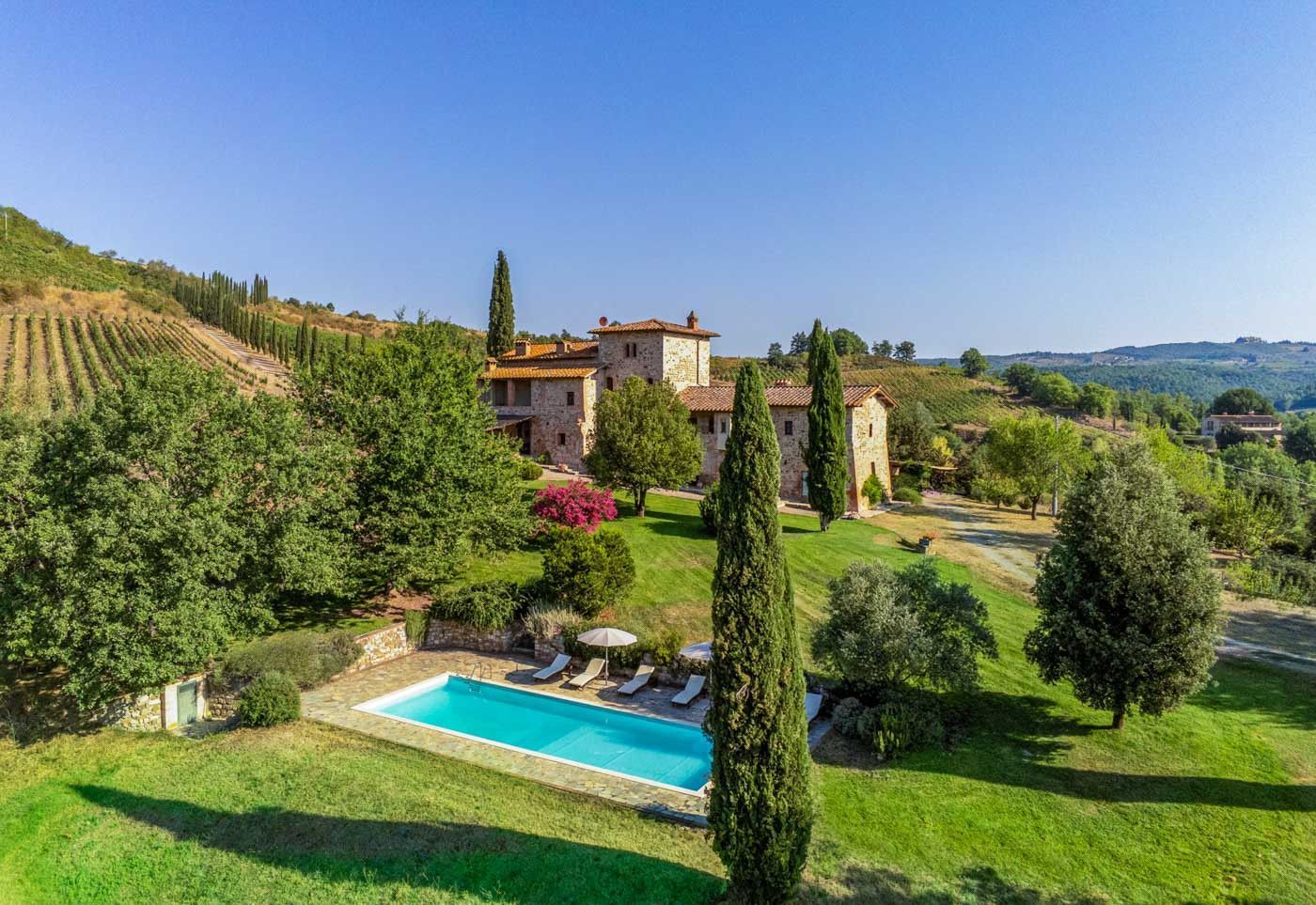 An aerial view of a large villa with a swimming pool in the middle of a lush green field in Tuscany.