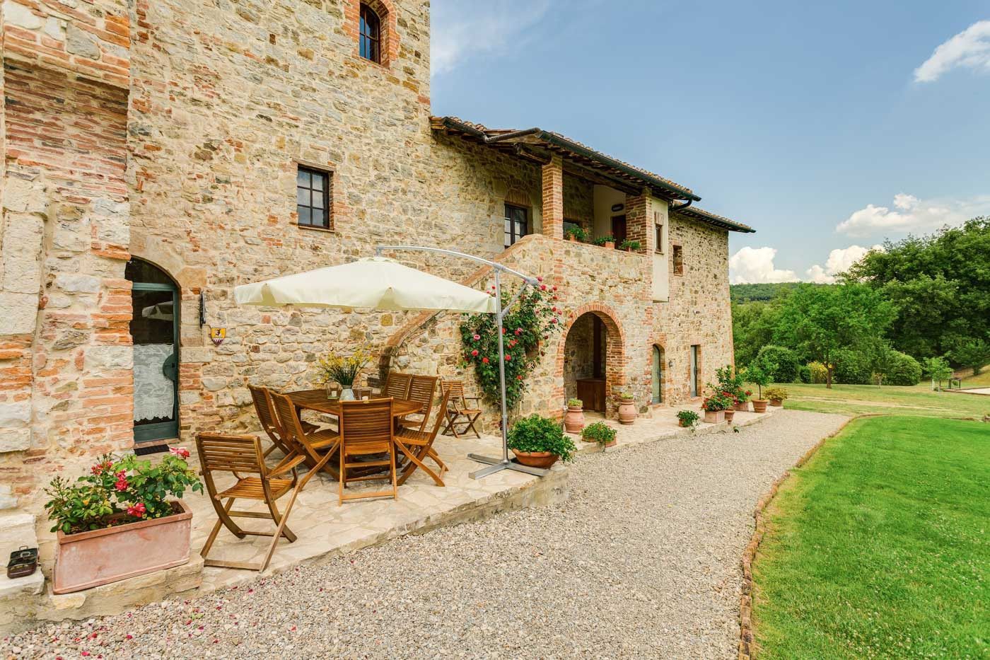 A stone villa with a patio area with a table and chairs and an umbrella in Tuscany.