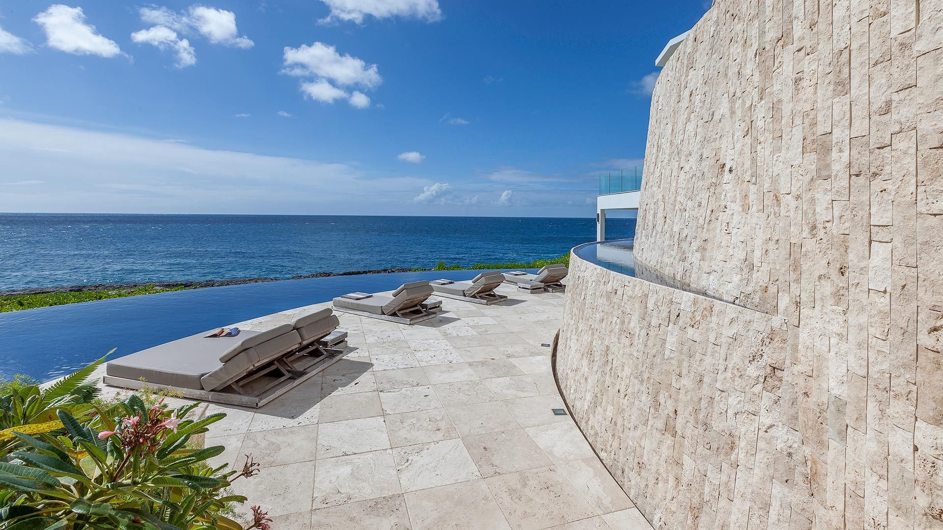 A swimming pool surrounded by a stone wall overlooking the ocean at villa in Antigua.