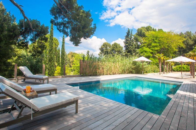 A large swimming pool surrounded by chairs and umbrellas on a wooden deck at villa in Cote D'Azur, France.