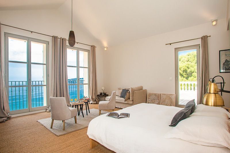 A bedroom with a large bed, chairs, and a balcony overlooking the ocean at villa in Cote D'Azur, France. 