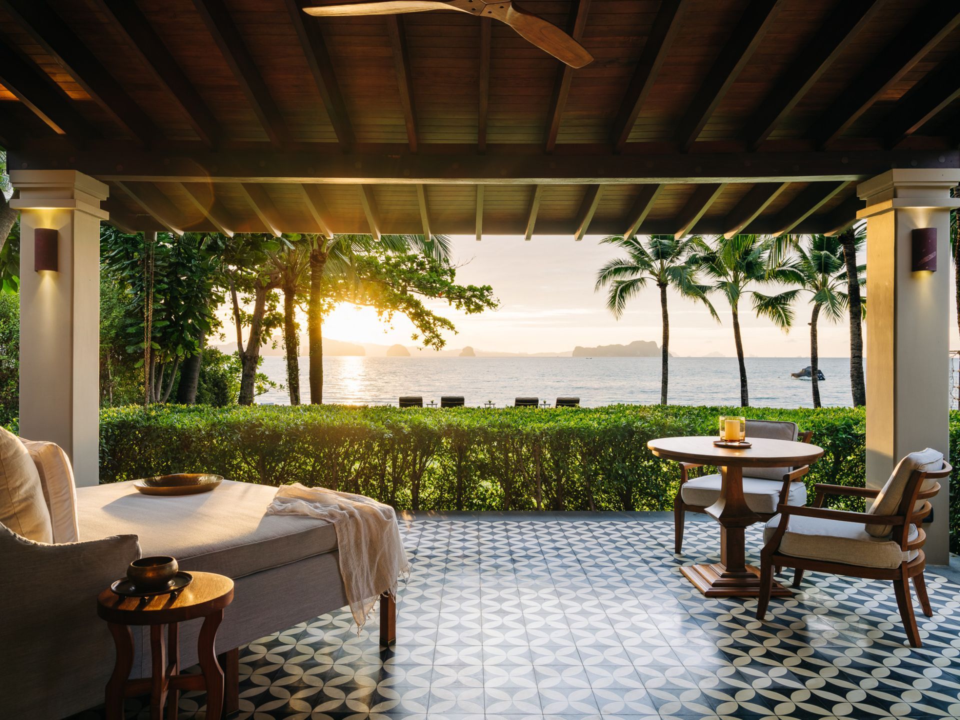 A patio with a bed, table, chairs, and a view of the ocean at villa in Koh Yao Noi, Thailand.