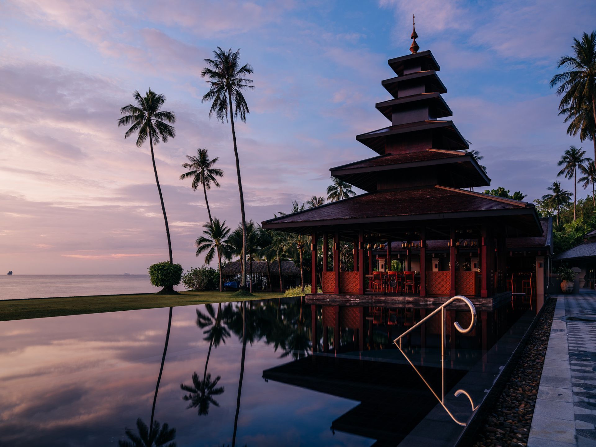 A pagoda villa is sitting next to a pool with palm trees in the background in Koh Yao Noi, Thailand.