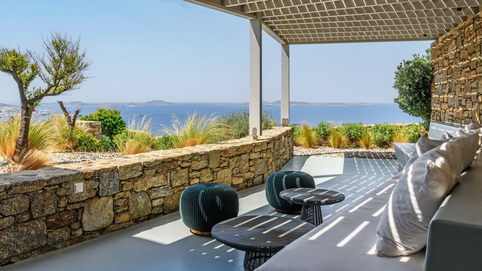 A patio with a couch, table, chairs, and a view of the ocean at villa in Mykonos, Greece.