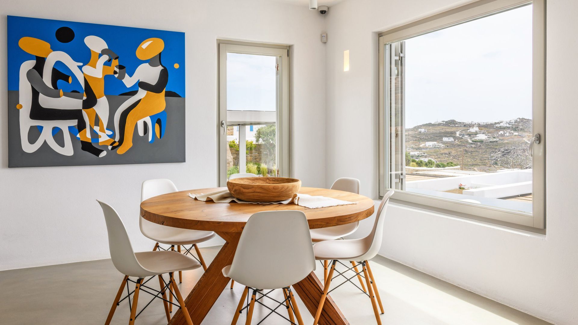 A dining room with a round table and chairs and a painting on the wall at villa in Mykonos, Greece.