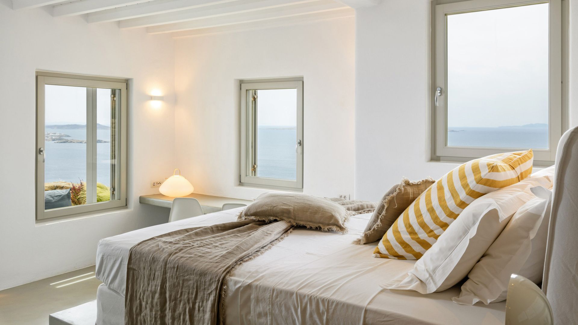 A bedroom with a bed , two windows and a view of the ocean at villa in Mykonos, Greece.