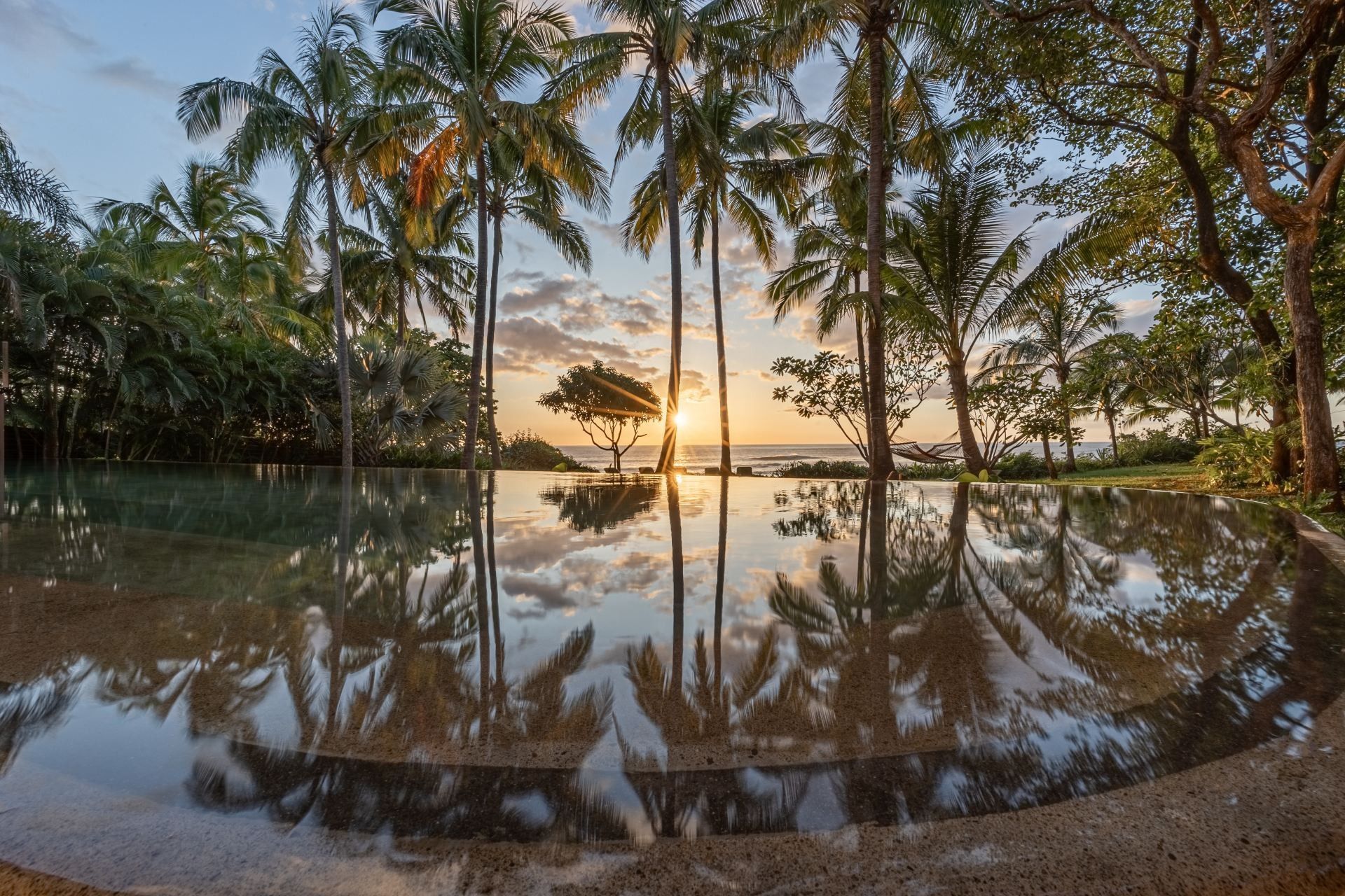 A swimming pool surrounded by palm trees at sunset at villa in Costa Rica.