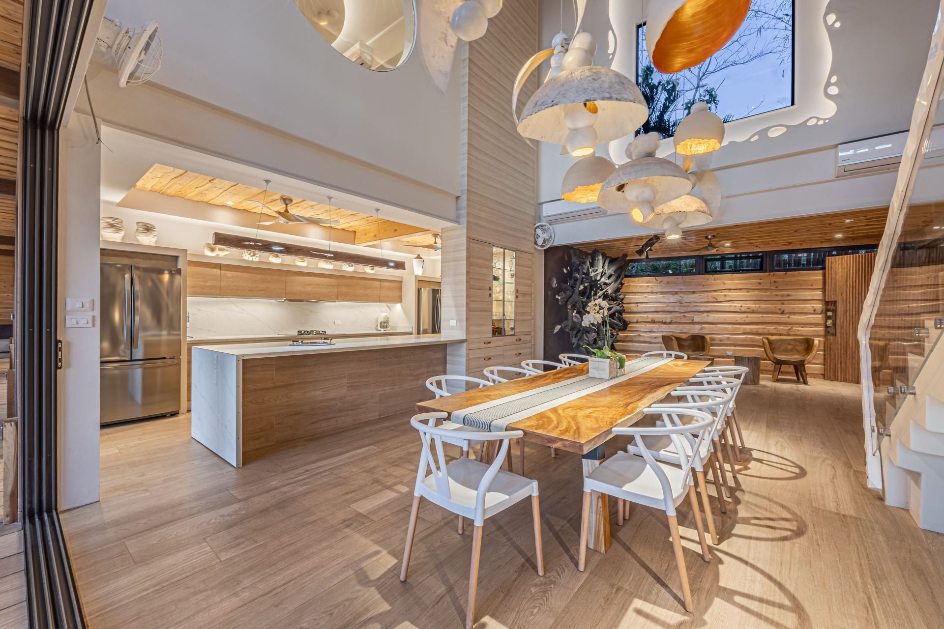 A dining room with a long table and chairs and a kitchen in the background at villa in Costa Rica.