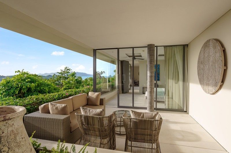 A balcony with a couch, chairs, and a table with a view of the ocean at villa in Koh Samui, Thailand.