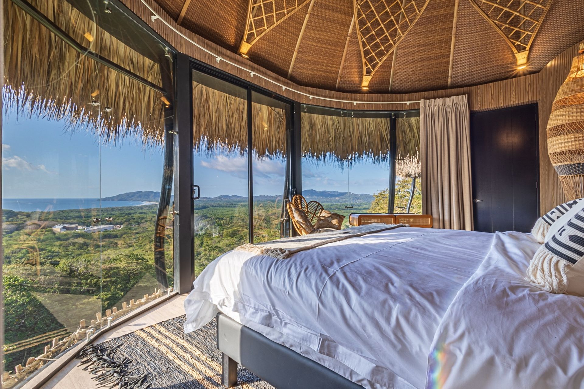 A villa with a thatched roof and a bed with a view of the ocean in Costa Rica.