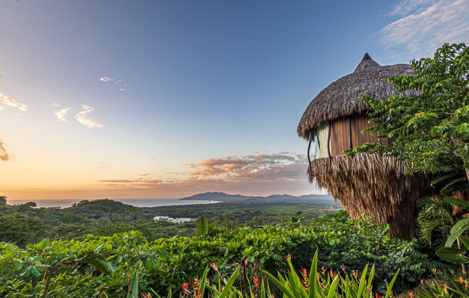 A thatched villa is sitting on top of a hill overlooking a lush green forest in Costa Rica.