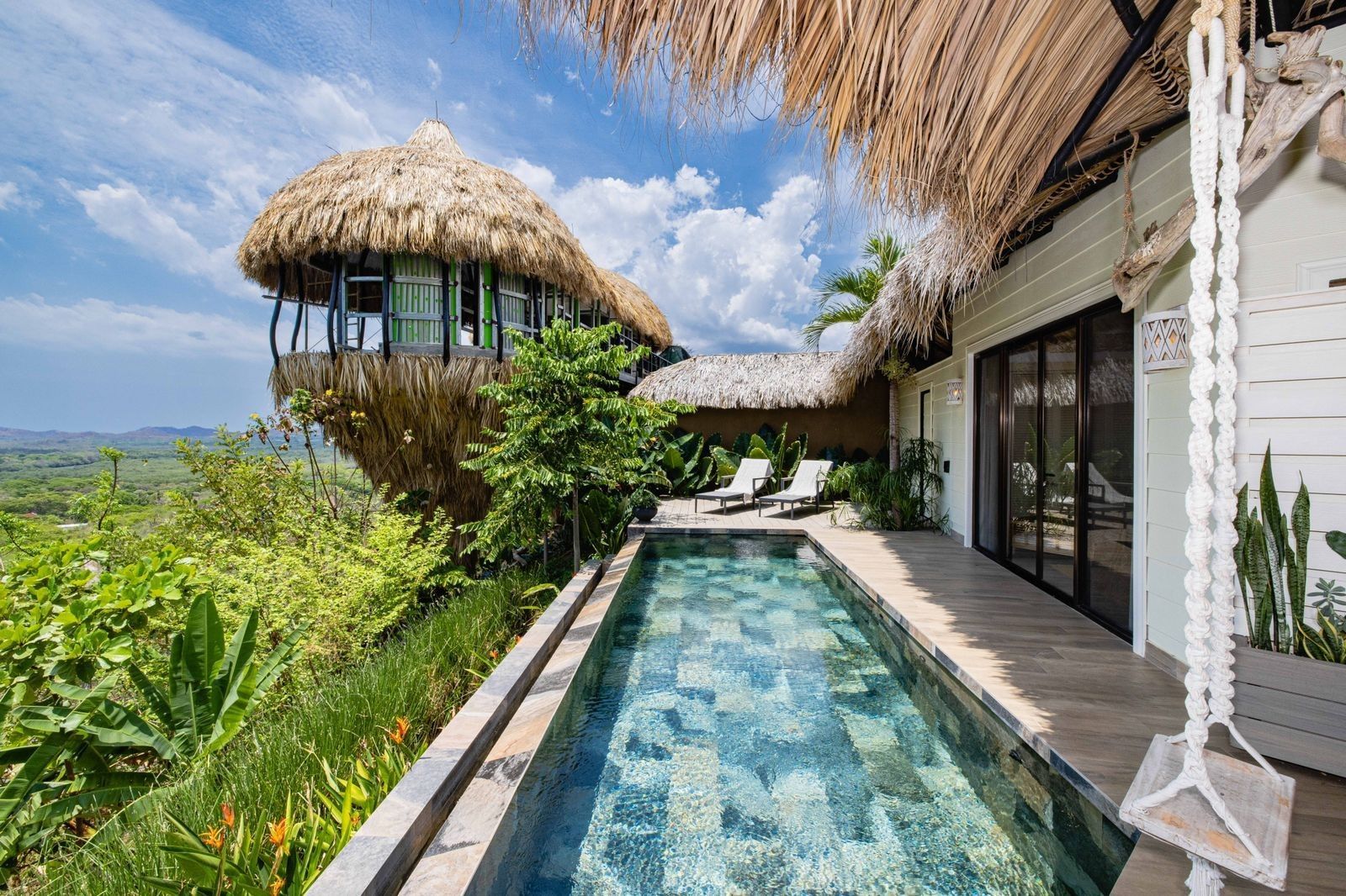 There is a swimming pool in front of a house with a thatched roof at villa in Costa Rica.