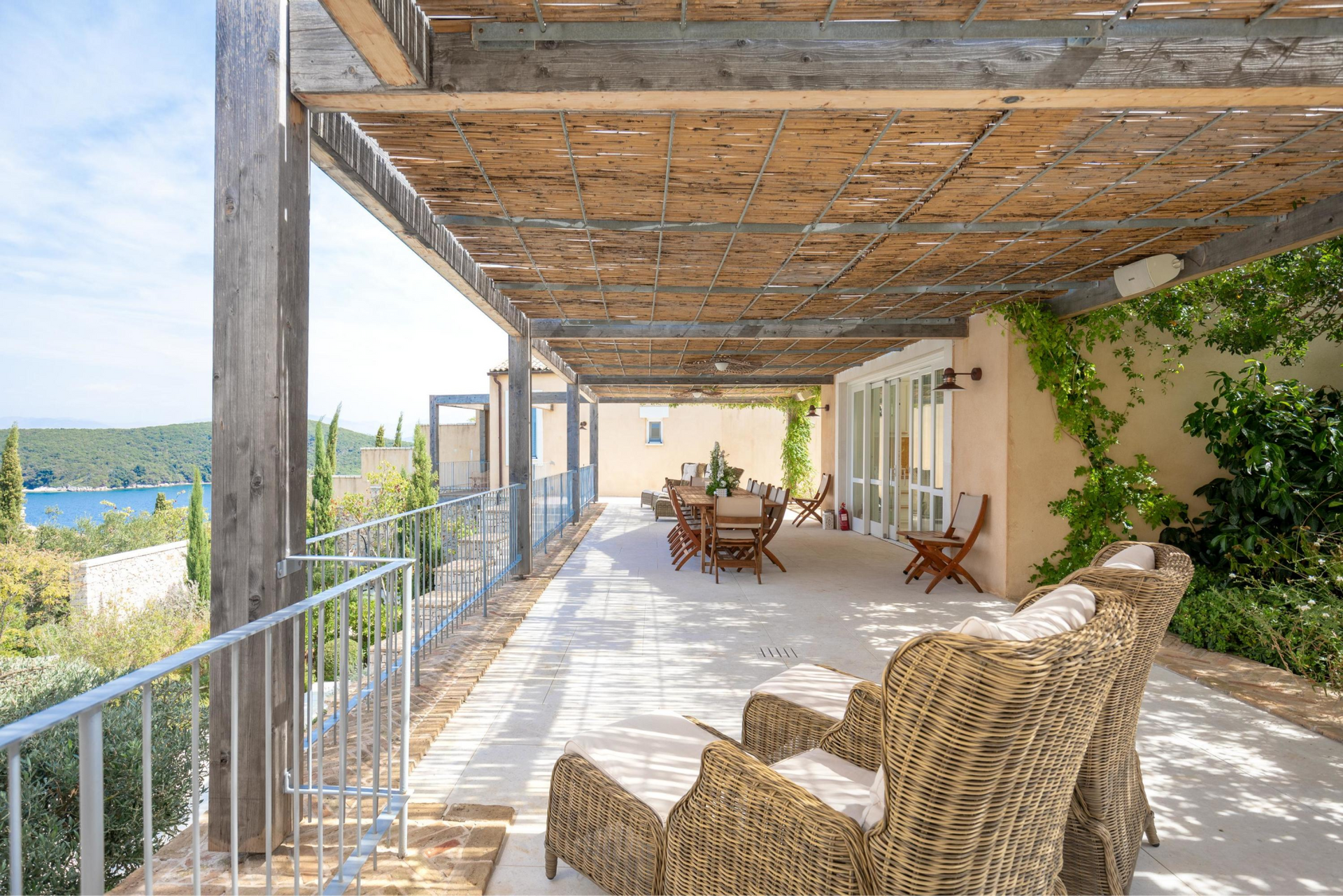 A large patio with wicker chairs and tables under a pergola. at villa in Corfu, Greece.