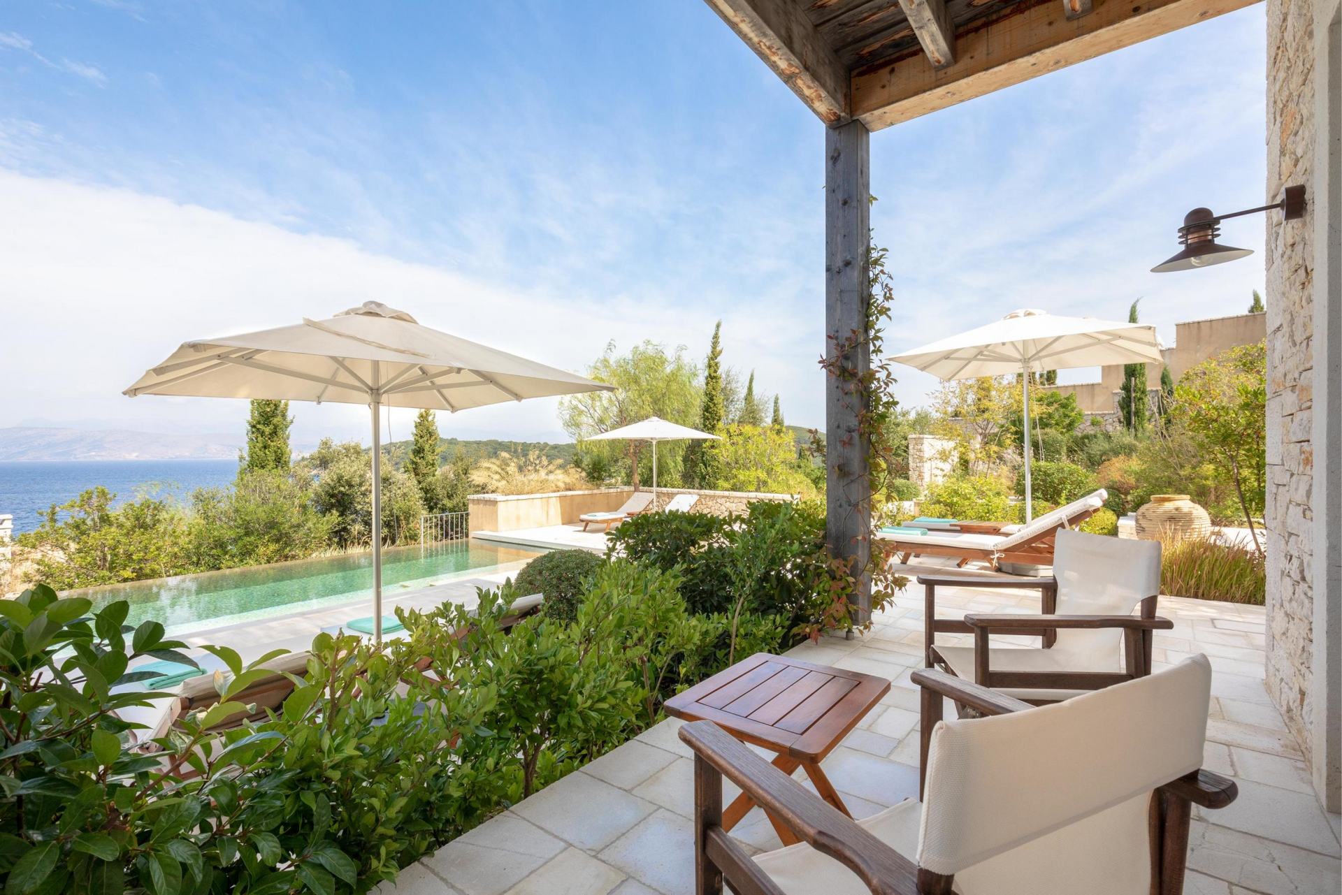 A patio with chairs and umbrellas overlooking a swimming pool at villa in Corfu, Greece.