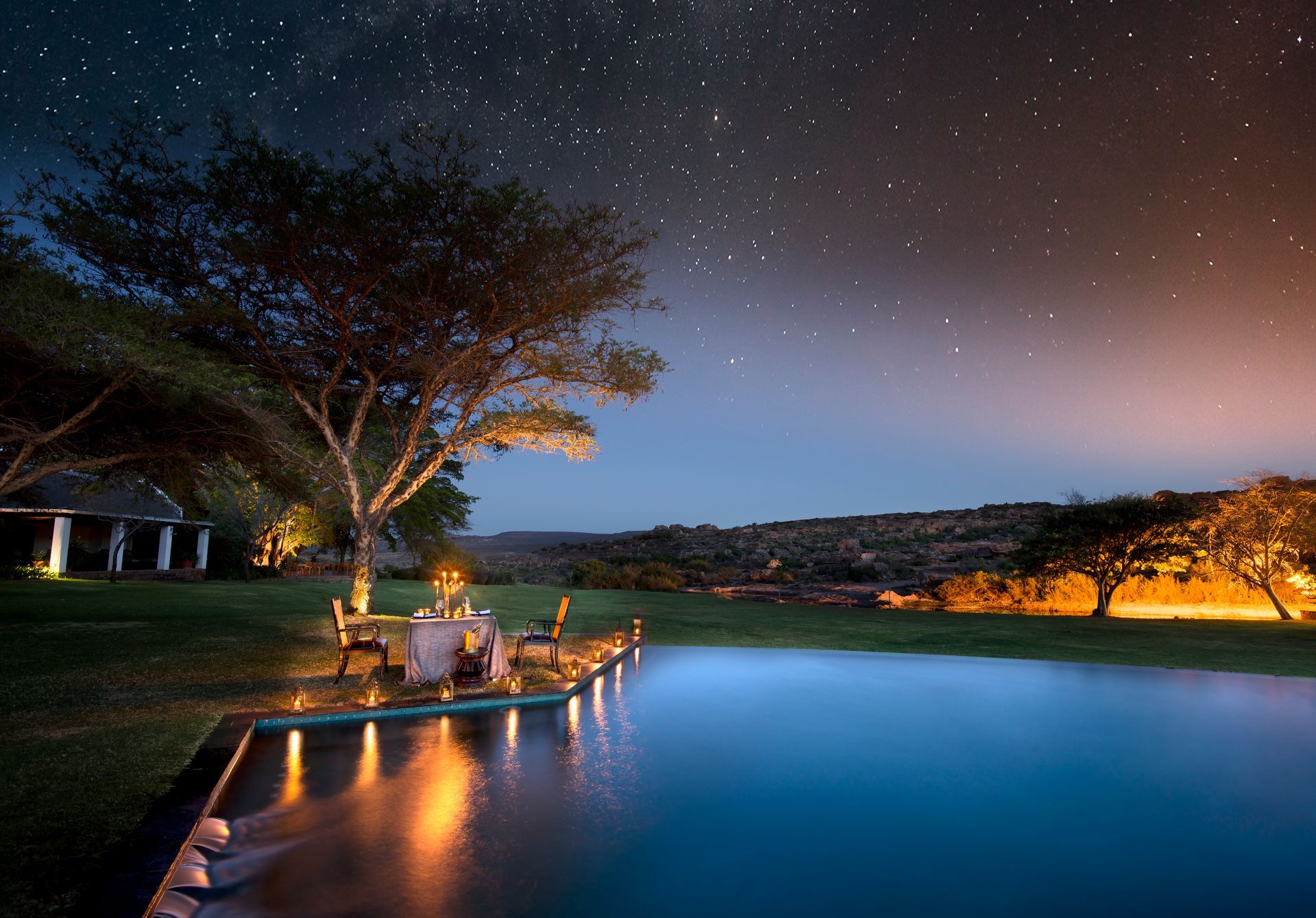 A swimming pool with a table and chairs under a starry night sky at the South Africa Red Carnation Hotel Collection