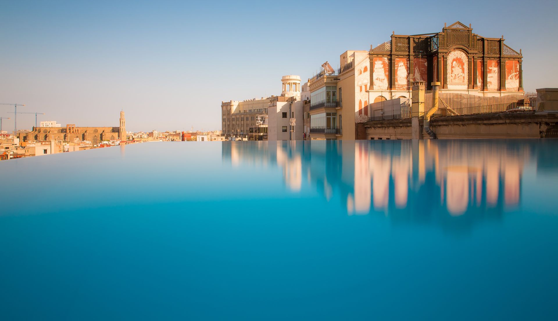 A large building is reflected in a large swimming pool at Grand Hotel Central in Barcelona, Spain.