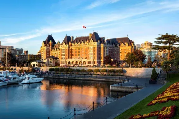 A large building is sitting next to a body of water with boats docked in front of it in Victoria, BC.