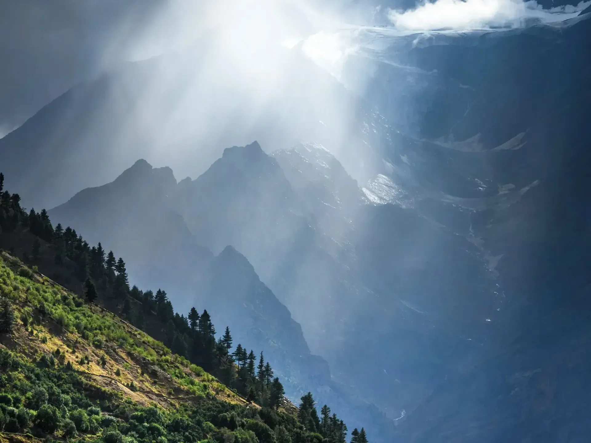 The sun is shining through the clouds on a mountain covered in trees in Bhutan.