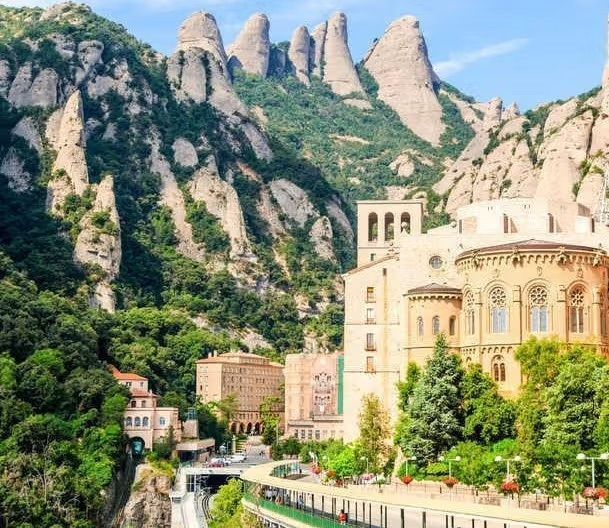 A large building is surrounded by mountains and trees in Catalonia, Spain.