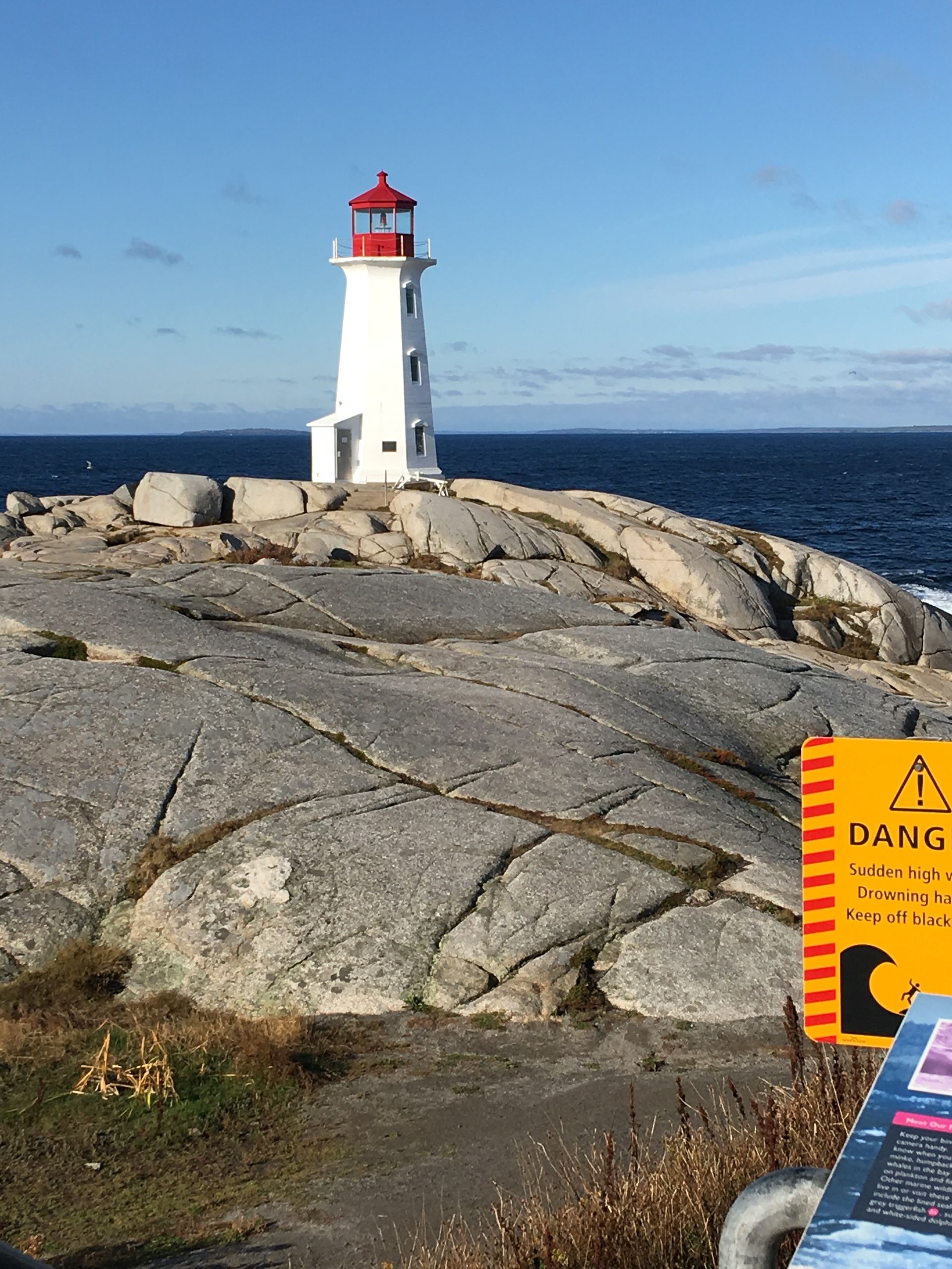 White lighthouse with red top on rocky coast; blue ocean and sky.