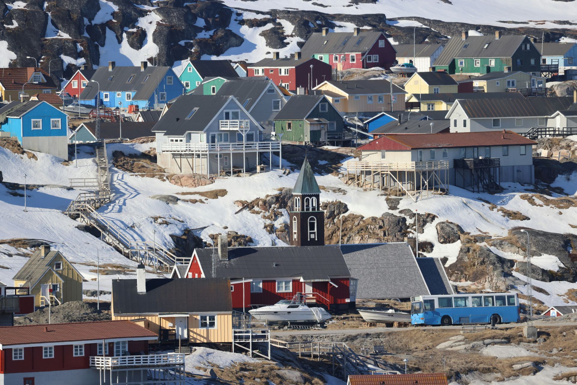 Colorful houses on a snowy hillside in the Greenland village of Ilulissat, with a church and bus visible.