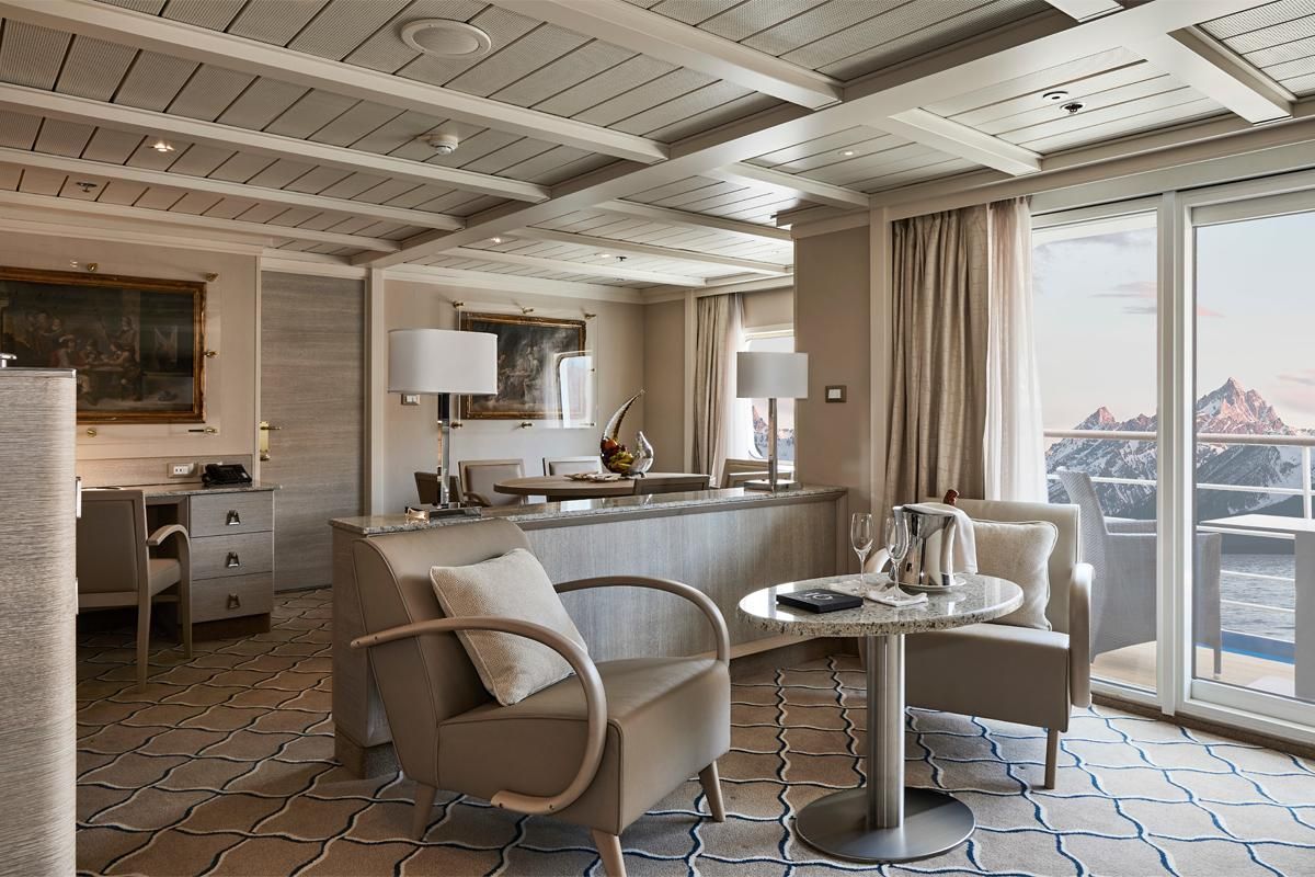 A living room with a table and chairs and a balcony on Silversea's Silver Cloud Expedition Cruise Ship.