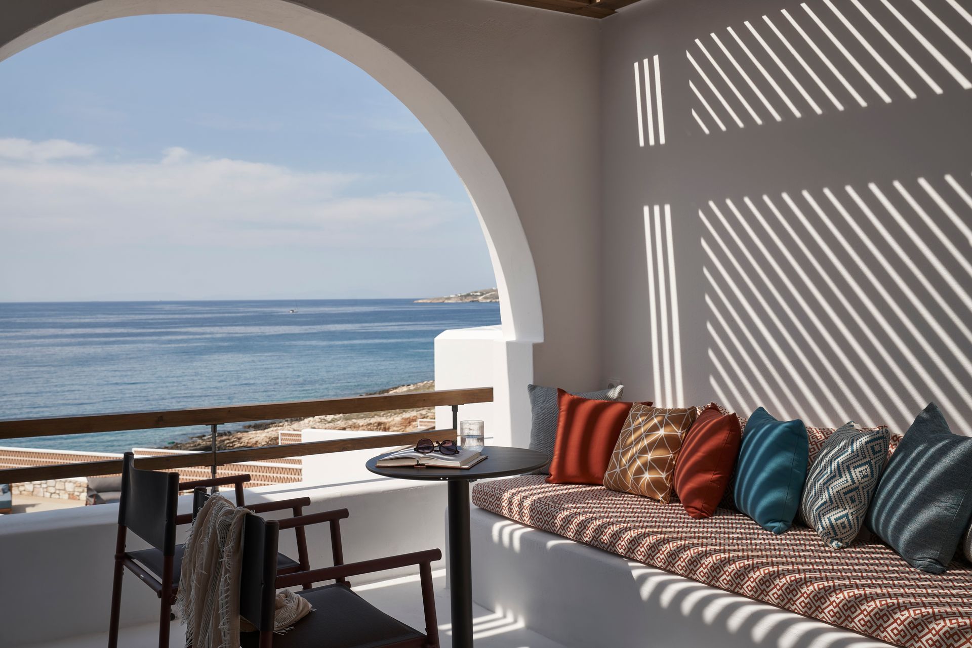 A balcony with a table and chairs overlooking the ocean at Andronis Minois Hotel in Paros, Greece.