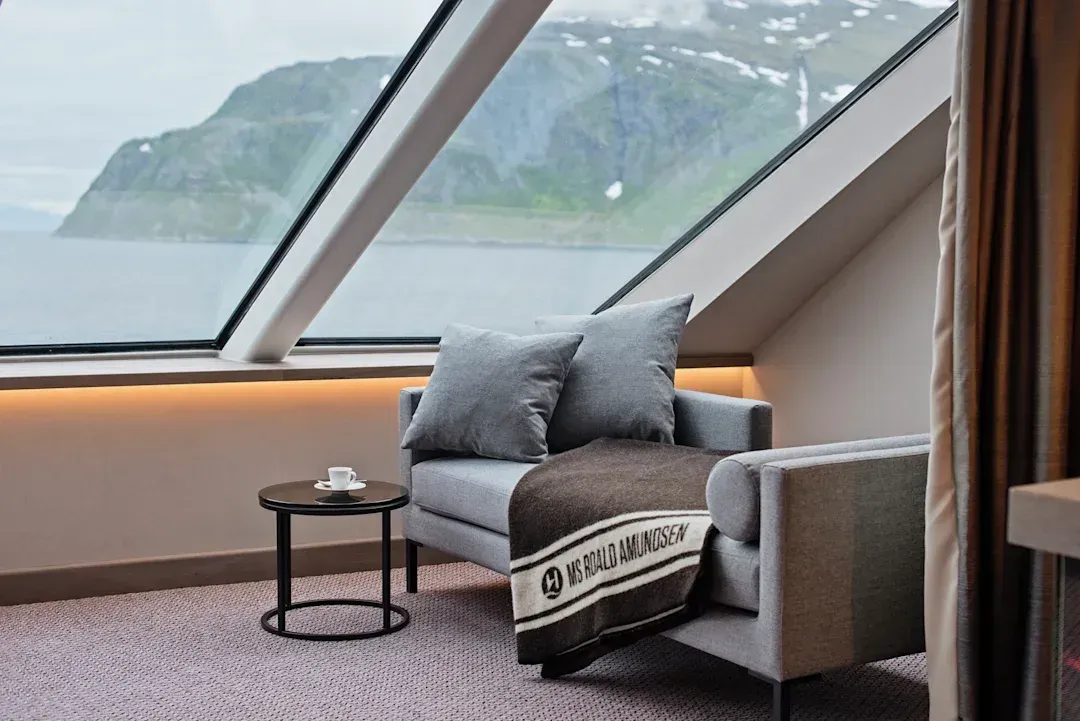 A chair with a blanket on it in a room with a large window on Hurtigruten Expeditions' MS Roald Amundsen cruise ship.