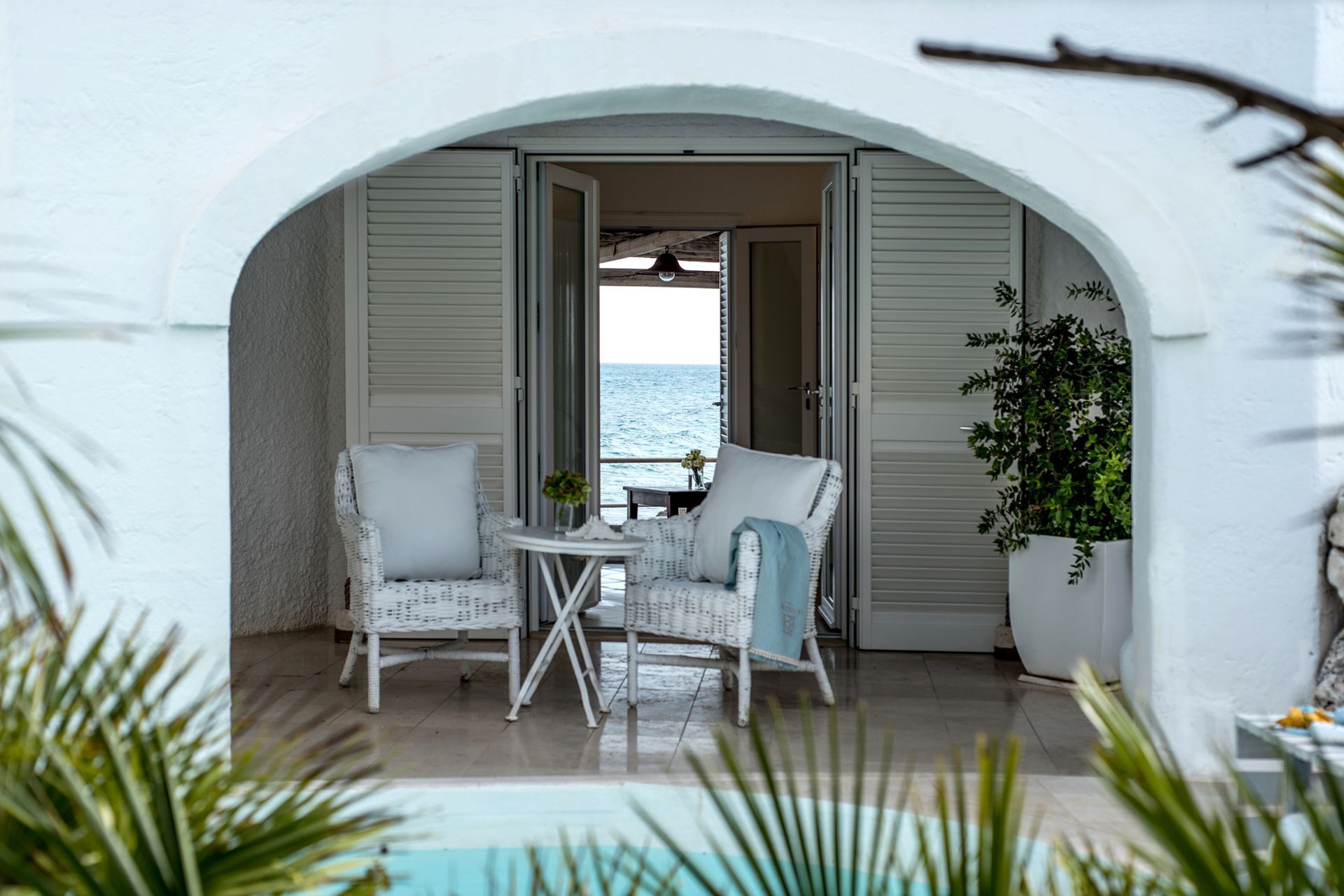 A balcony with chairs and a table overlooking the ocean at La Peschiera Hotel in Puglia, Italy.