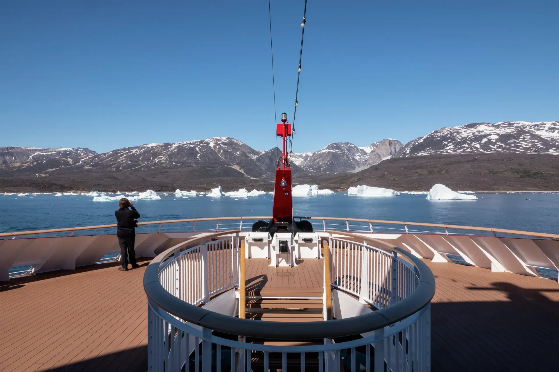 A man is standing on the deck of a cruise ship, looking at icebergs in the water on the MS Fridtjof Nansen cruise ship.