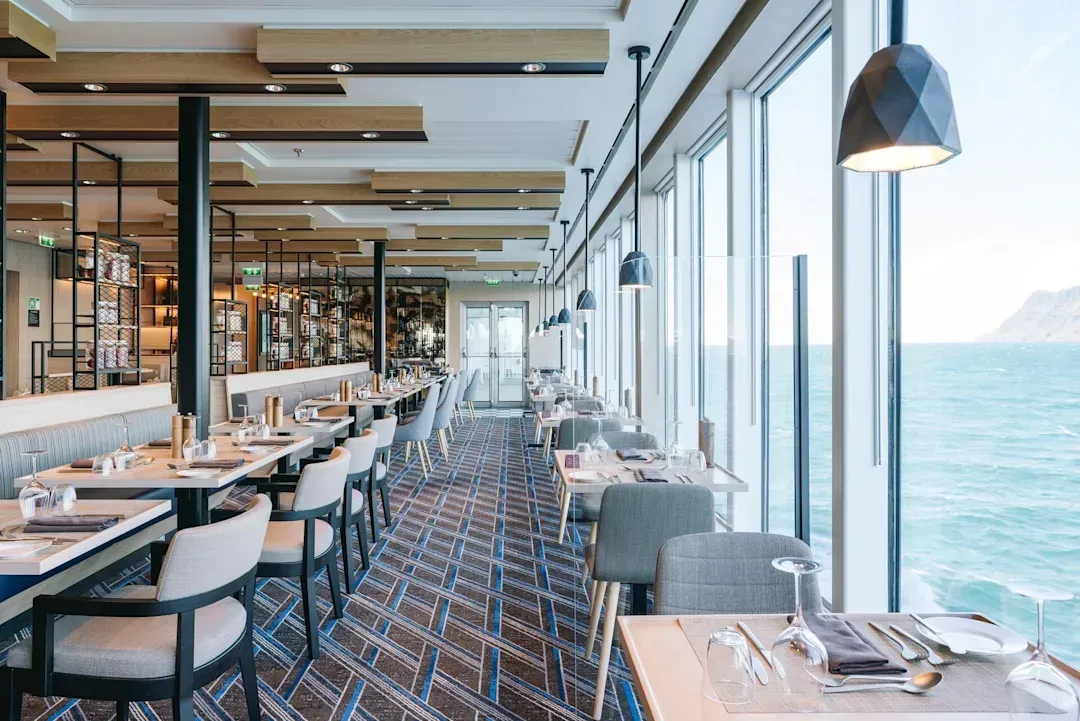 A restaurant with tables and chairs and a view of the ocean on Hurtigruten Expeditions' MS Roald Amundsen cruise ship.