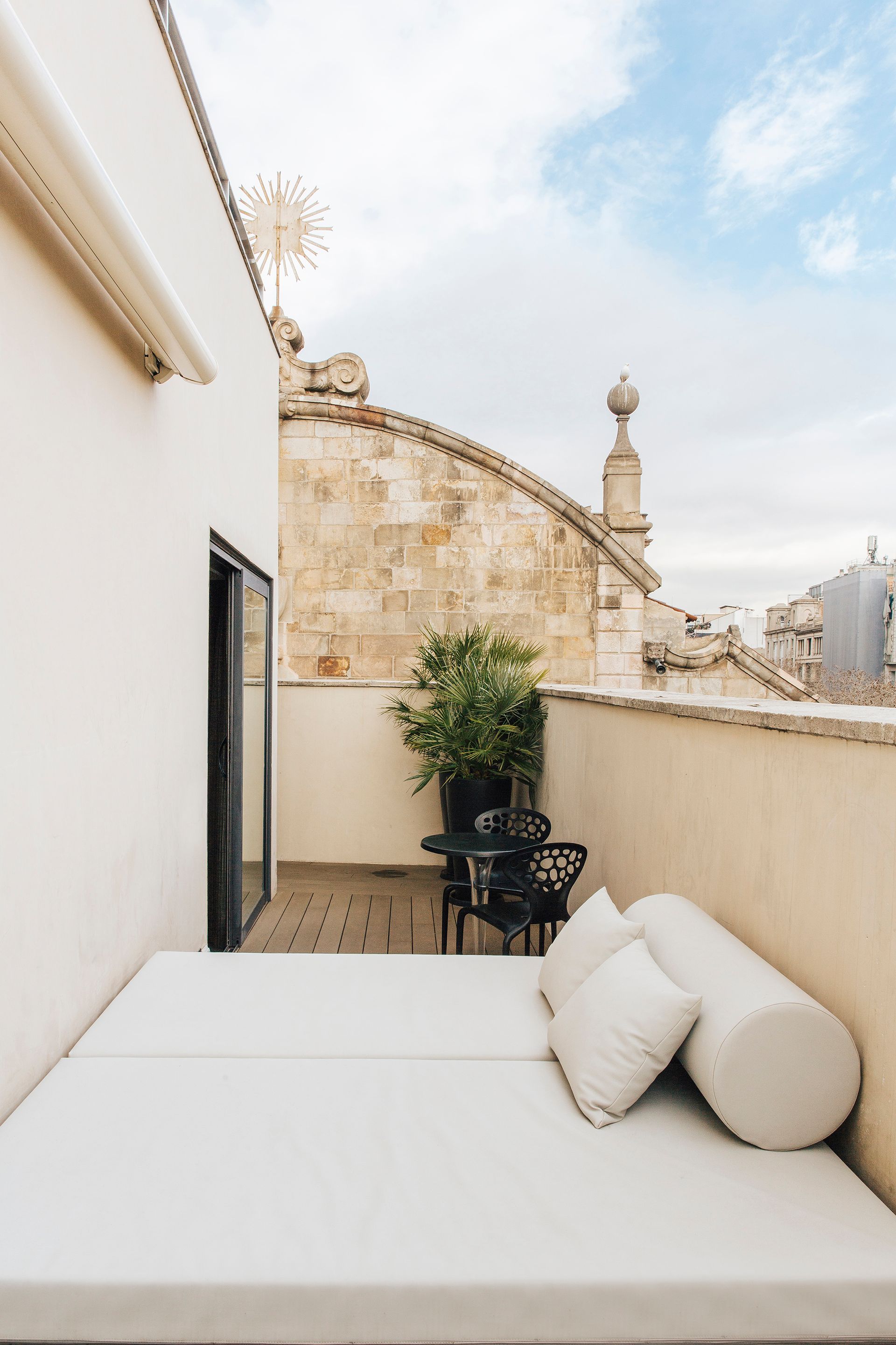 There is a large bed on the balcony with a table and chairs at Hotel Bagués in Barcelona, Spain.