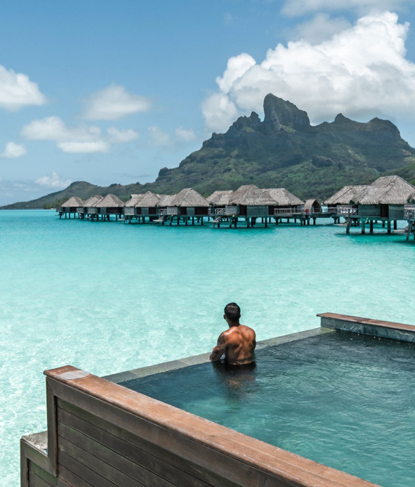 A man is in an infinity swimming pool in an overwater bungalow overlooking bora bora at four seasons. 