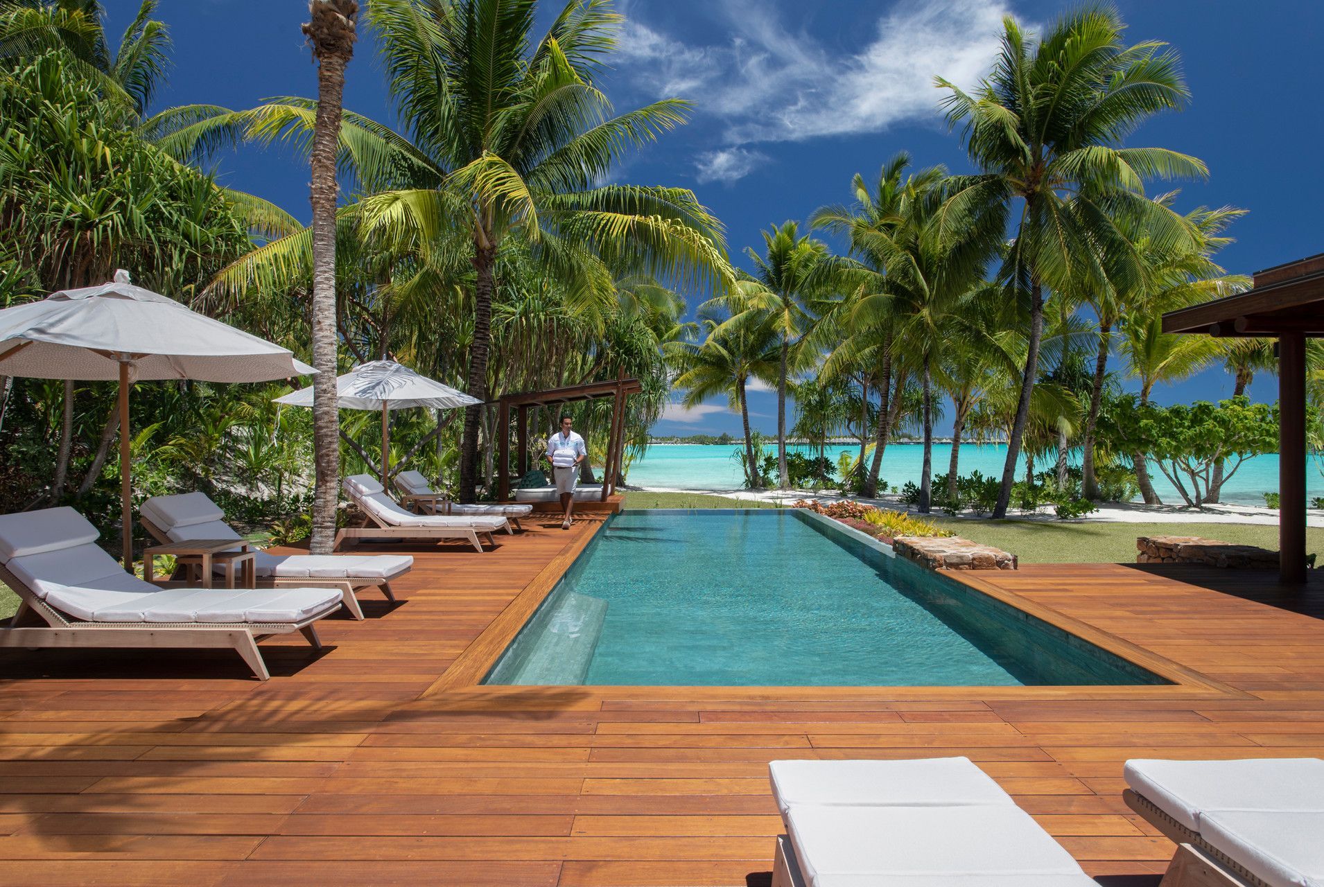 A large swimming pool surrounded by chairs and umbrellas on a wooden deck in Bora Bora at Four Seasons Resort.