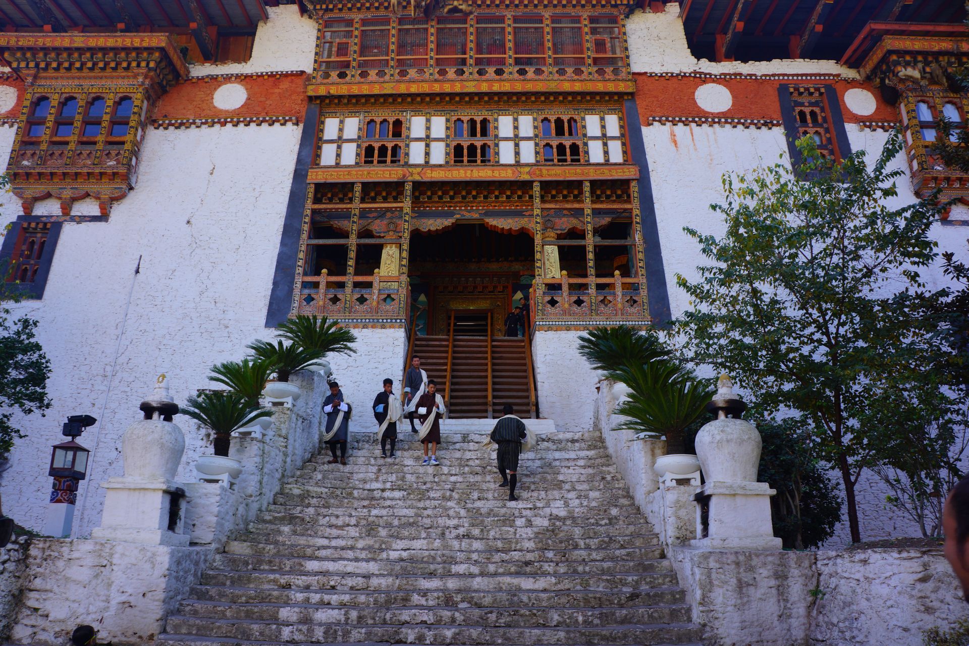 A group of people walking up stairs in front of a large building in Bhutan.