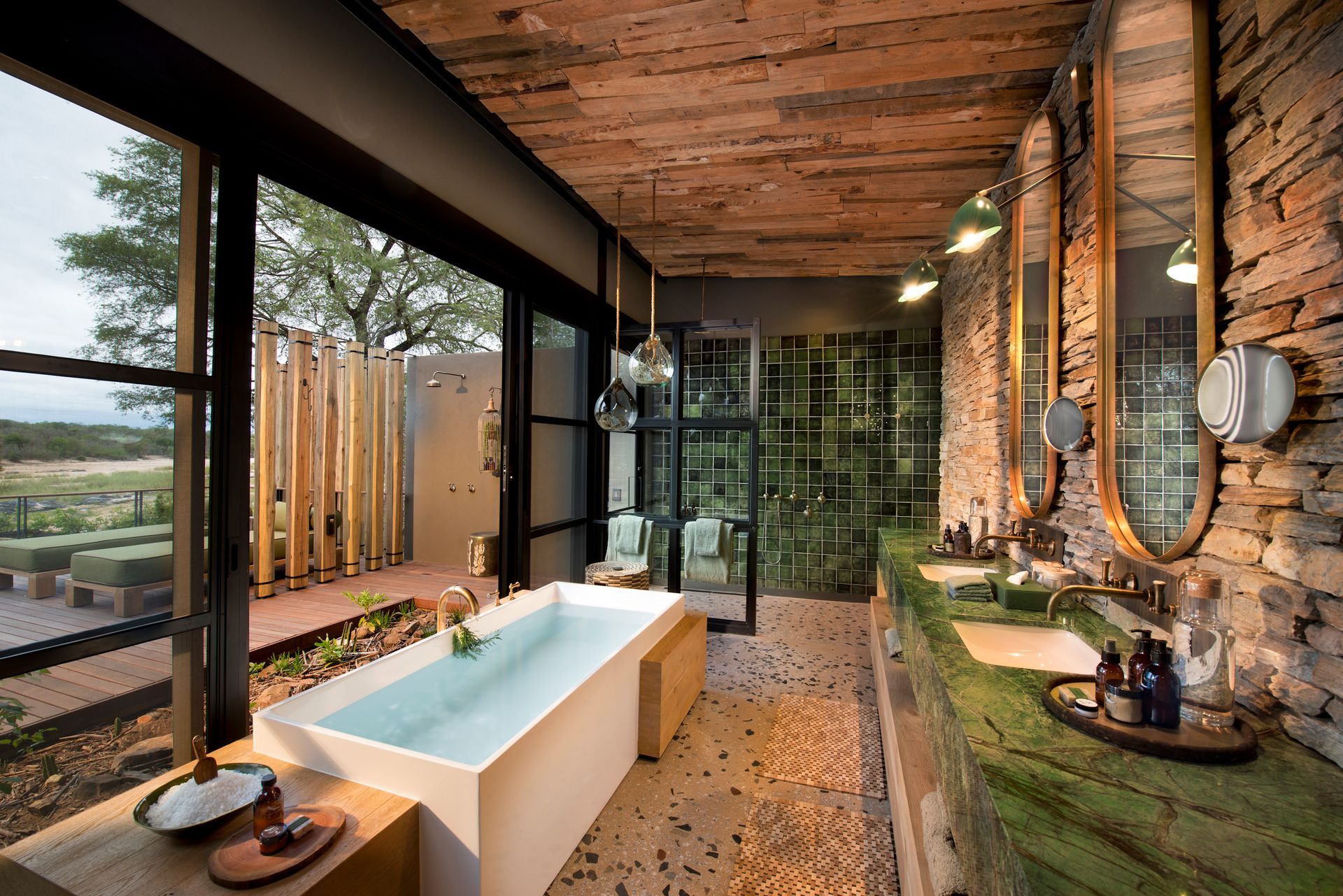 A bathroom with a bathtub, sinks, mirrors, and a large window at a lodge in Africa.