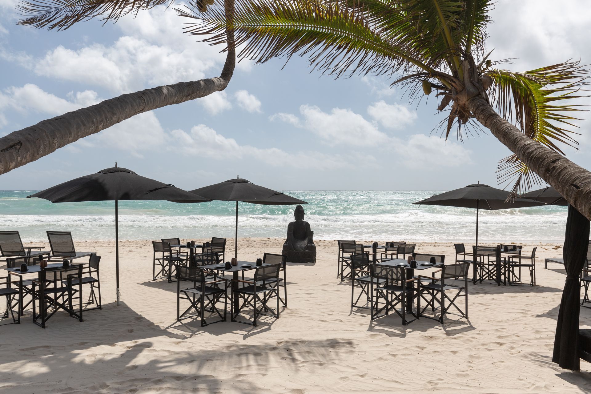 A beach with tables and chairs and black umbrellas at TAGO Tulum Hotel in Mexico.