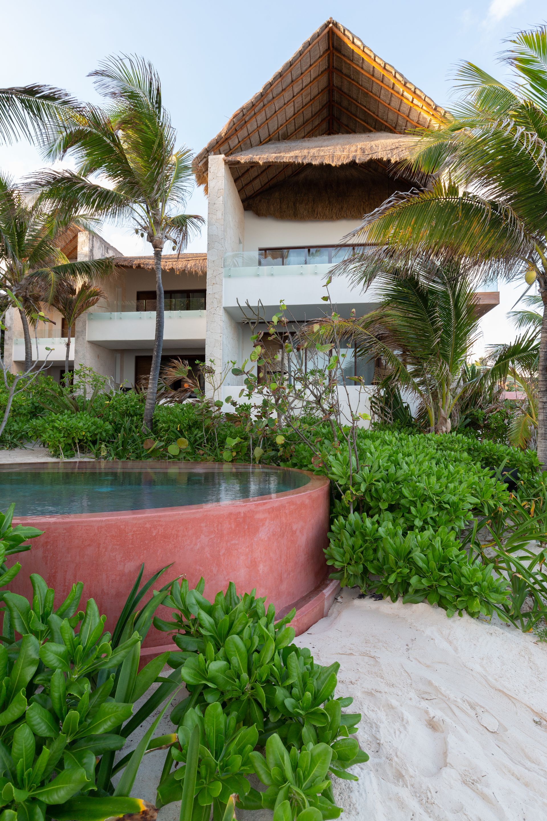 A large house with a thatched roof and a swimming pool in front of it at TAGO Tulum Hotel in Mexico.