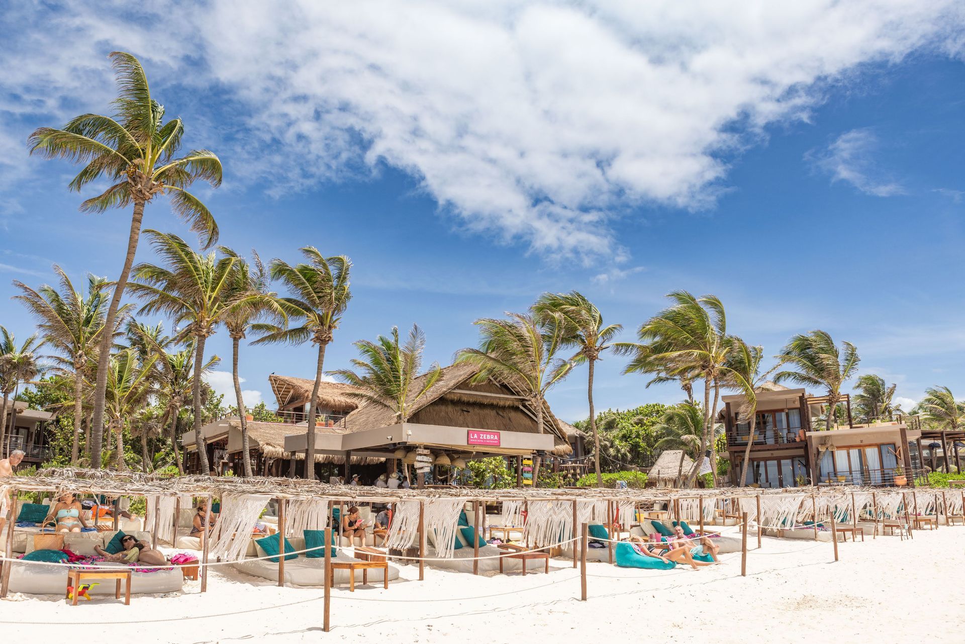 A beach with palm trees and a building in the background at La Zebra hotel in Tulum, Mexico.