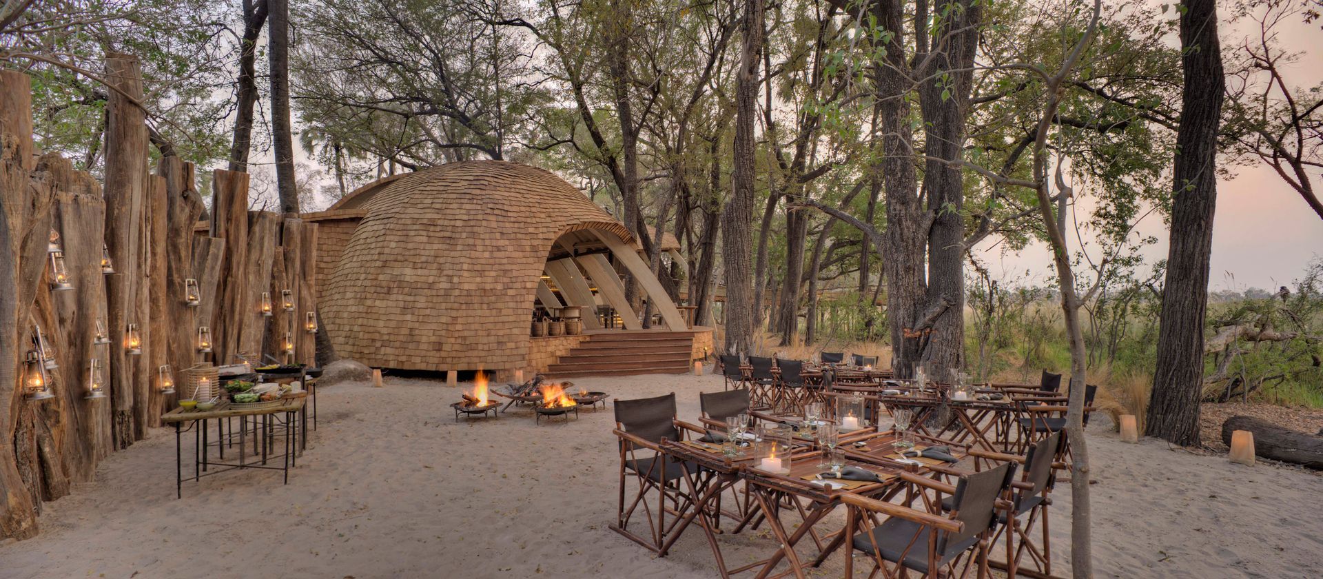 A dining area in the middle of a forest with tables and chairs at a camp in Africa.