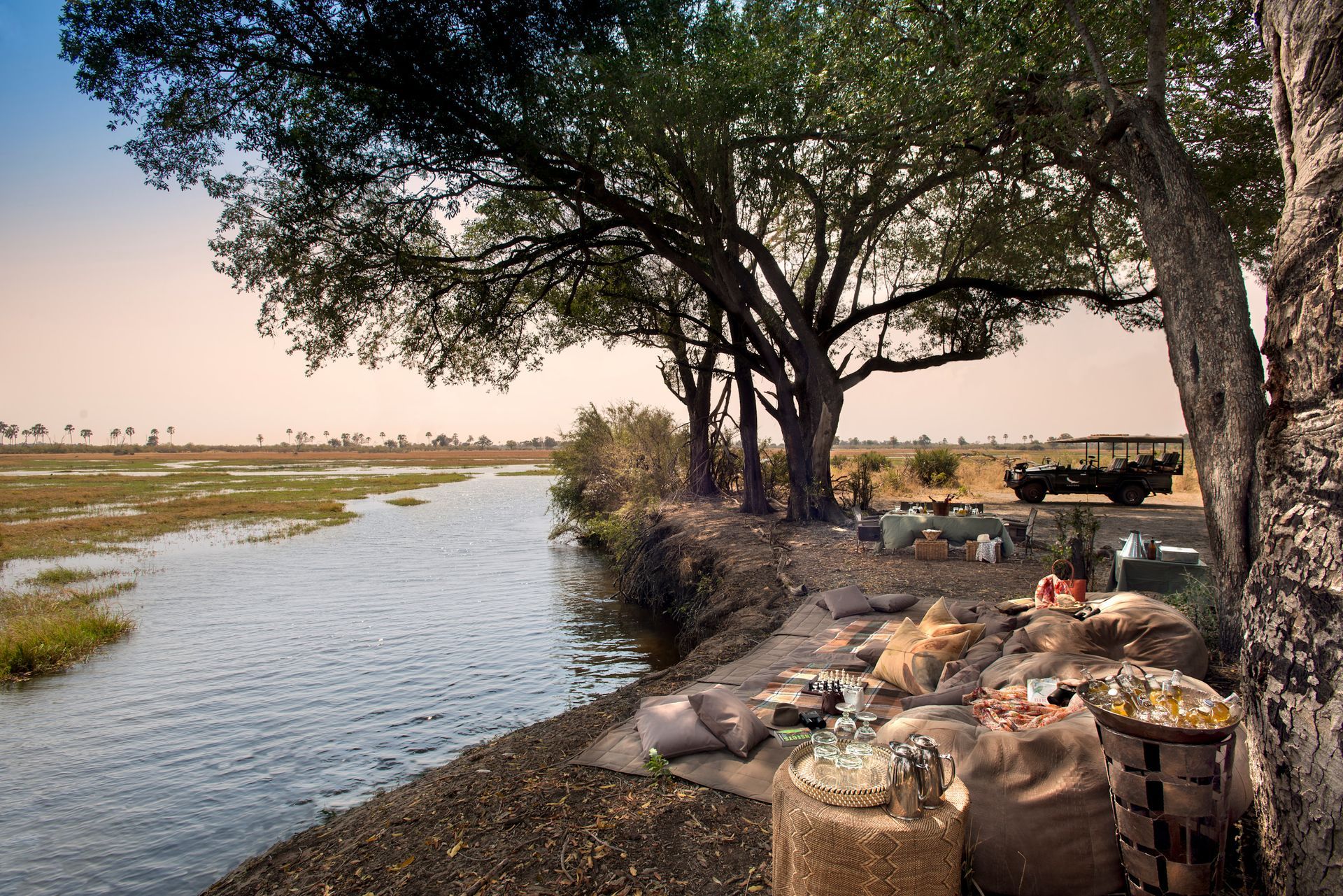 A picnic area next to a river with a jeep in the background at a camp in Africa.