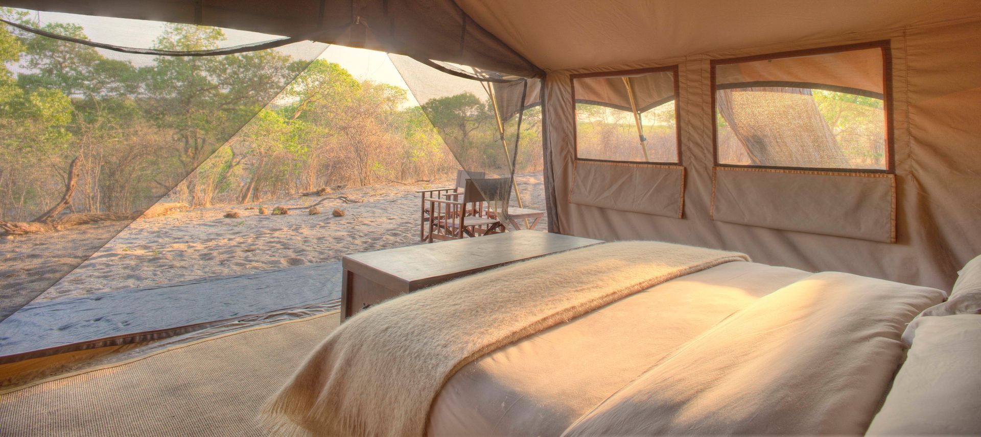 A bed in a tent with a view of a field at a camp in Africa.