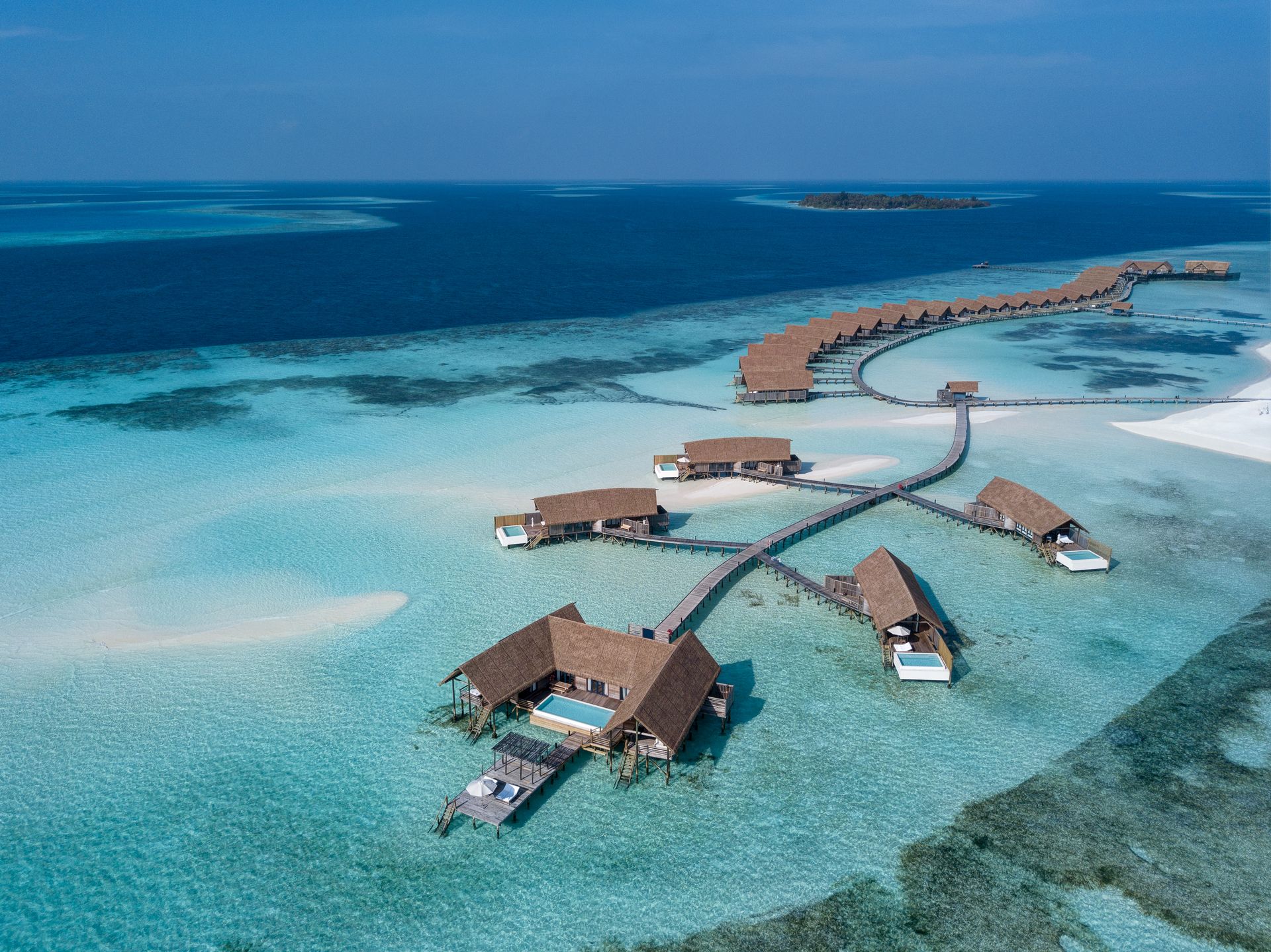 An aerial view of the Maldives with a strip of COMOs over the water bungalows. 