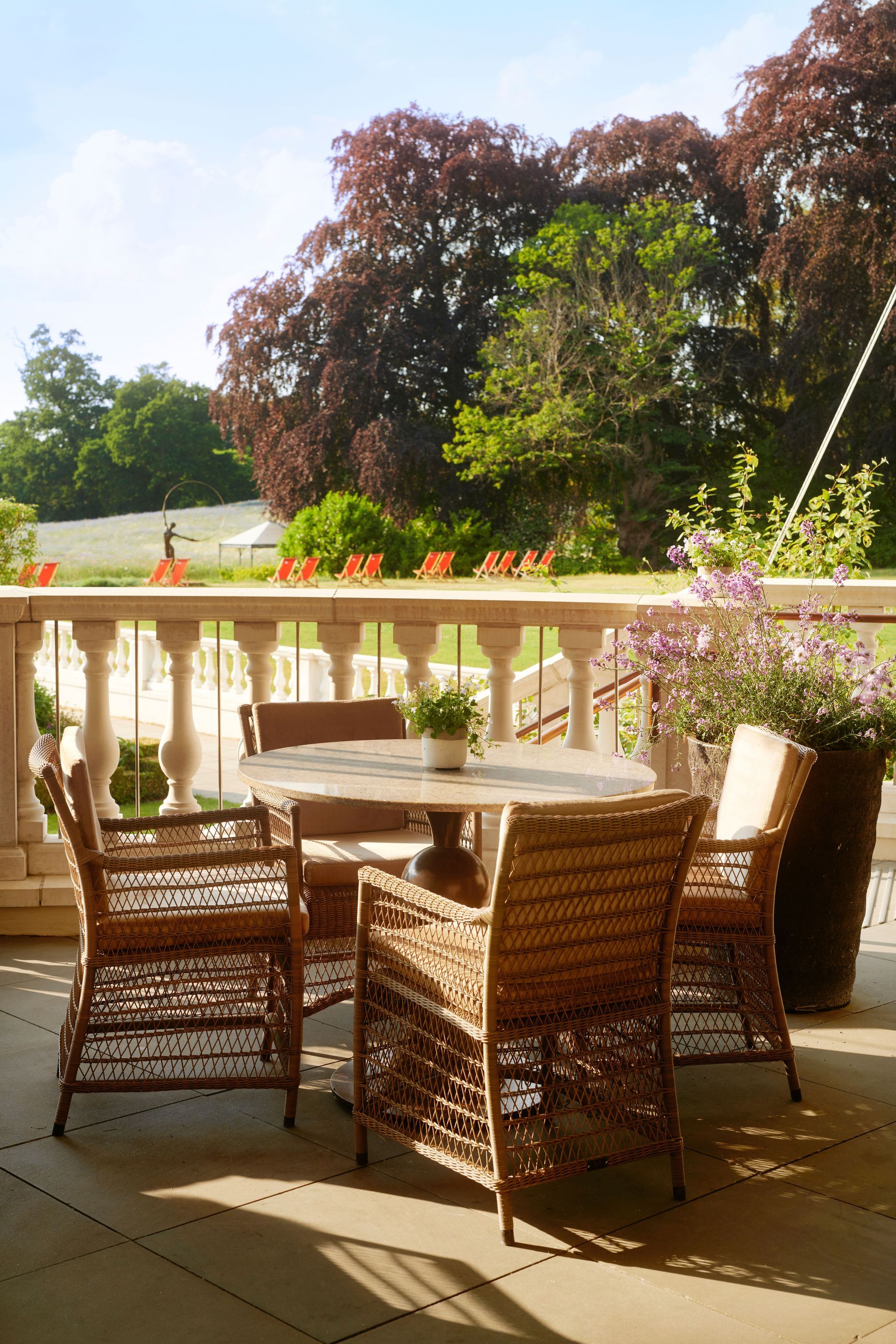 A table and chairs on a balcony with trees in the background at the Dorchester Collection Hotel in Ascot, UK