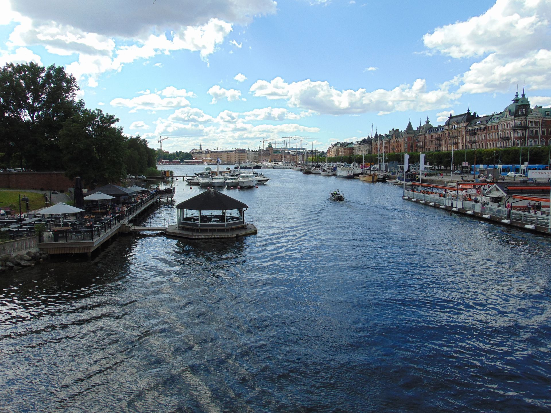 Waterway with boats, docks, and buildings under a blue sky with clouds.
