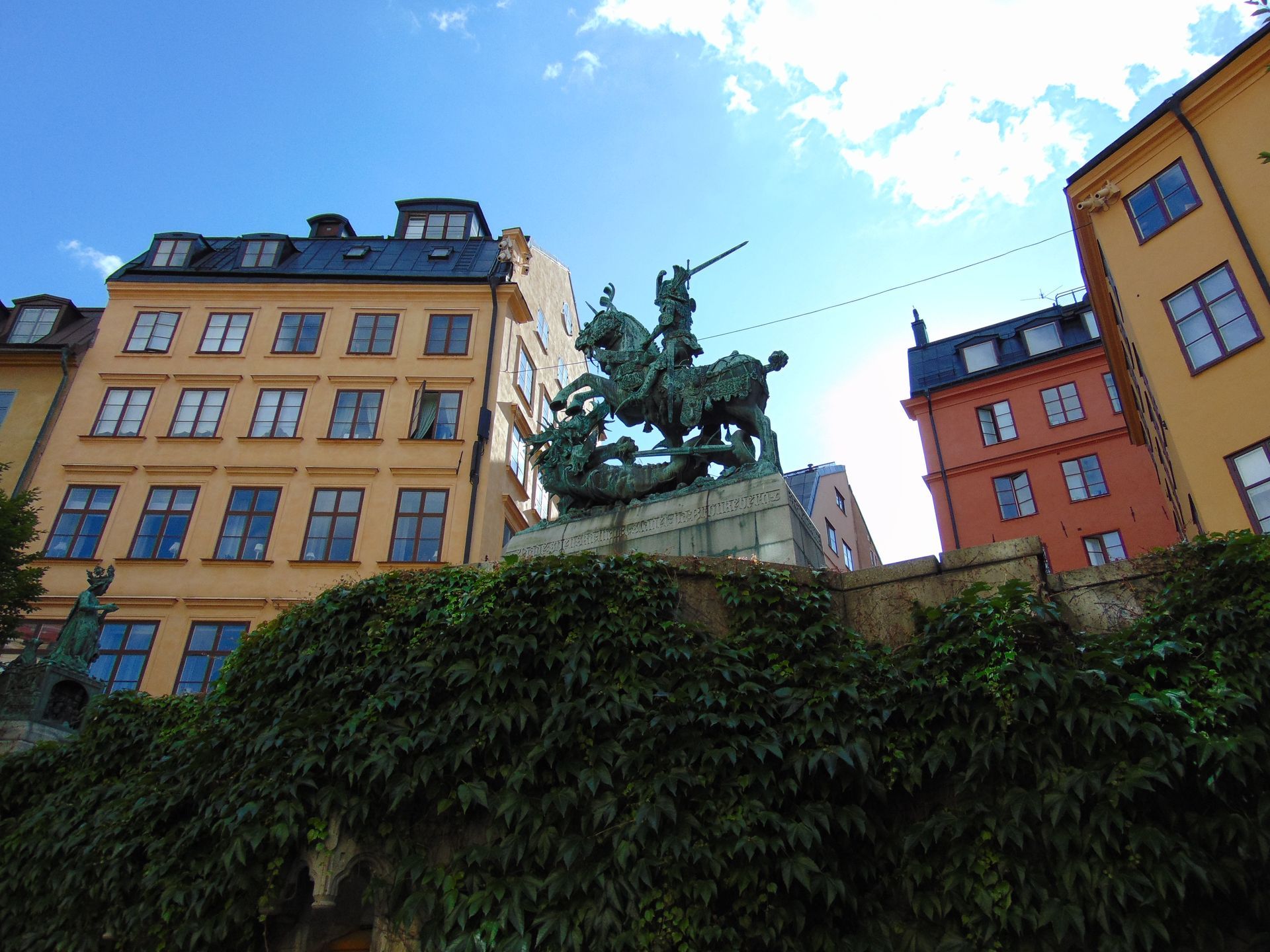 Bronze statue of Saint George on horseback slaying a dragon in Stockholm, Sweden, in front of buildings.